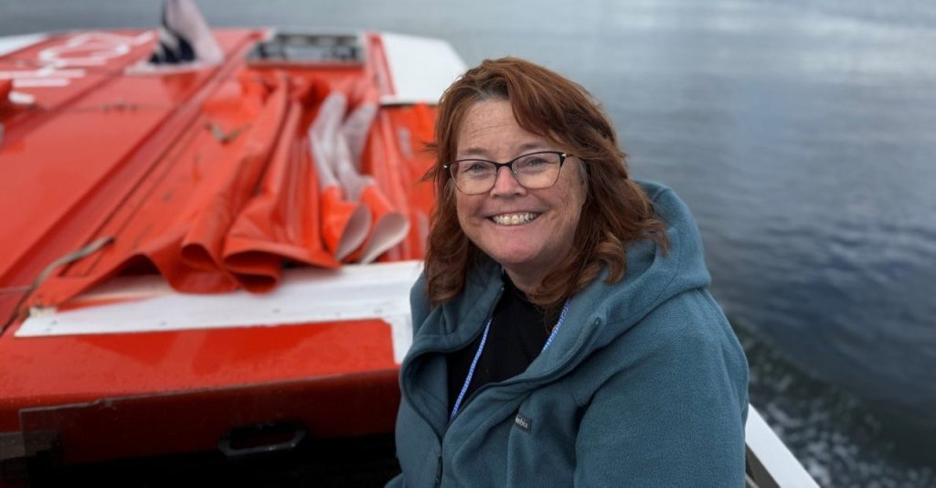 Kari smiles in her green fleece jacket as she sits on the tender from the ship to the shore.