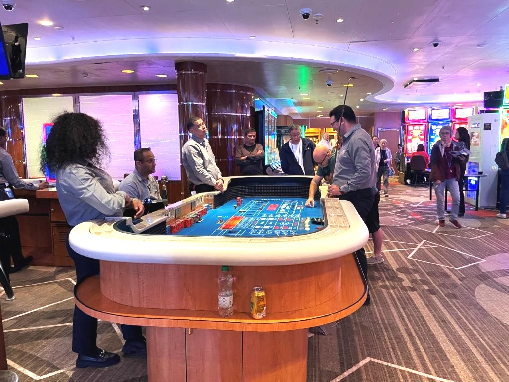 Slot machines and gaming tables fill the casino beneath colorful lighting and patterned carpet. The casino is open while the ship is at sea and offers both table games and electronic machines.