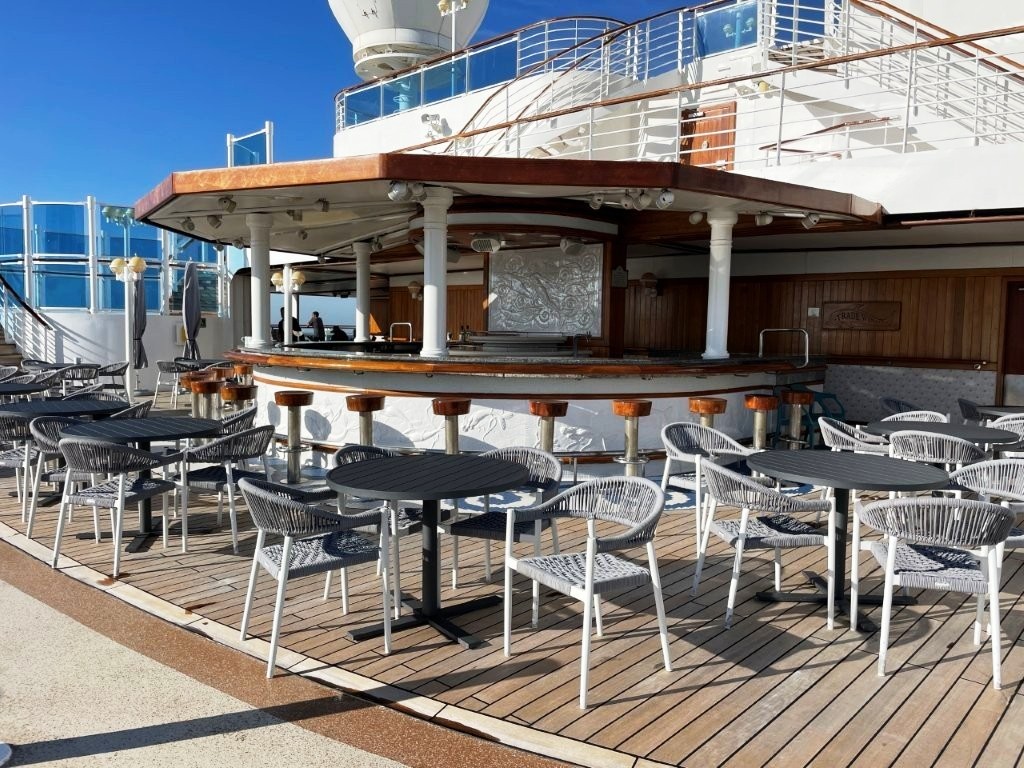 A covered bar sits beside the outdoor pool with bar stools and tables facing the deck. It's an easy place to grab a drink without leaving the pool area.