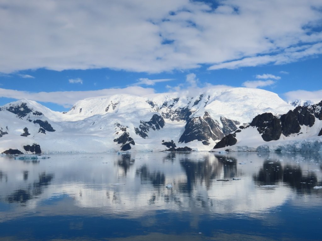 Snow-covered mountains and dark rocky peaks reflect across calm Antarctic water. Every hour brought a slightly different combination of light, clouds, ice, and reflections.