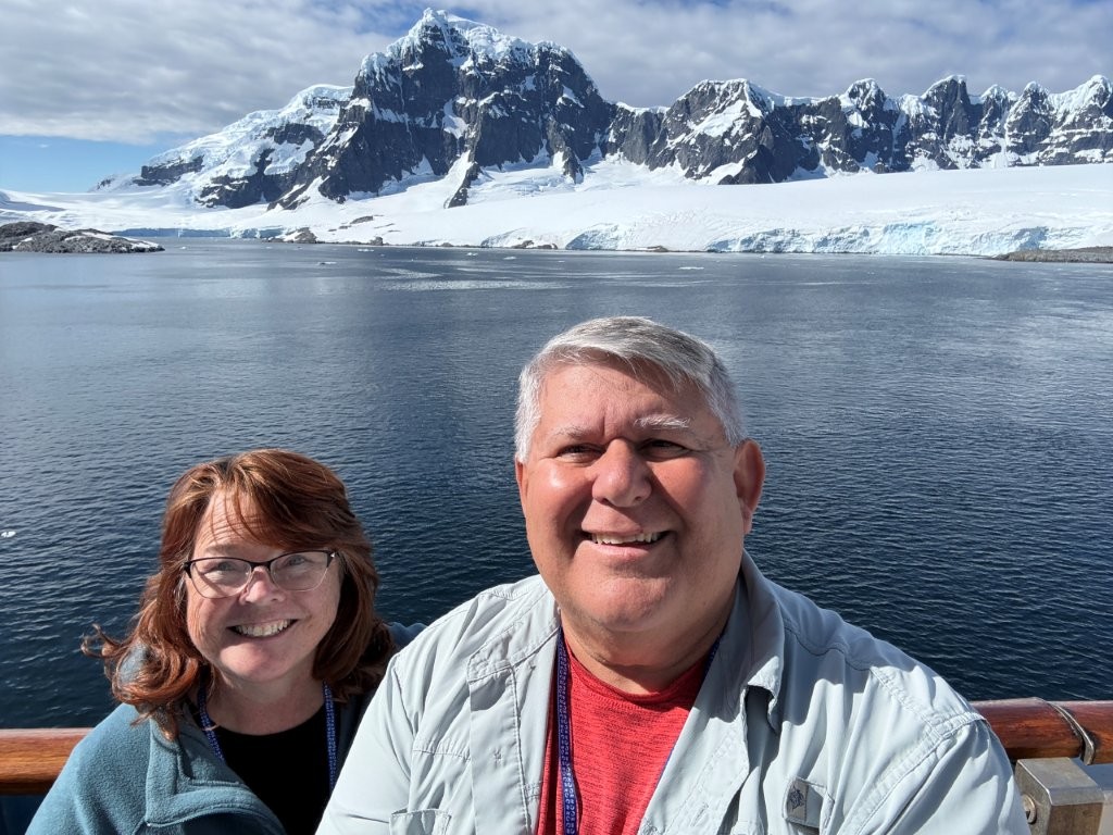 Kari and Bill smile together with Antarctica's dramatic mountains, glaciers, and floating ice filling the background. Thoughtful packing meant they could focus on the incredible scenery instead of worrying about being cold.