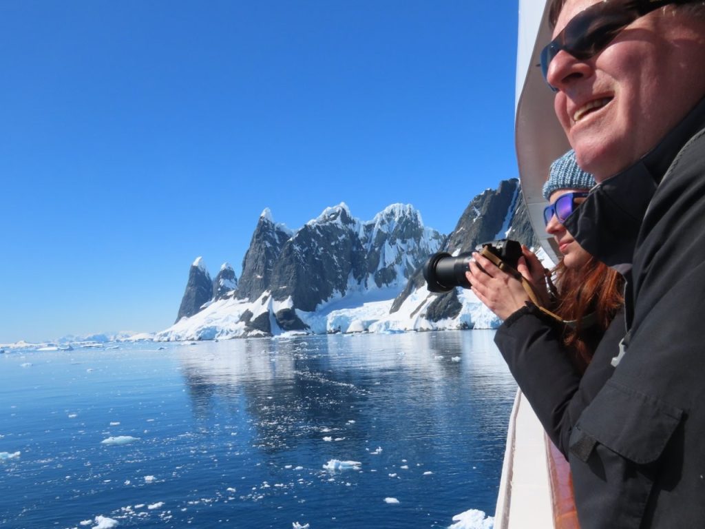 A woman holds her camera beside the ship’s railing with dramatic Antarctic mountains in the background. Photography was one of my biggest priorities, and scenic cruising let me keep my camera ready without managing Zodiac gear.