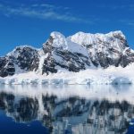 Snow-covered Antarctic mountains reflect perfectly in calm blue water beneath a bright sky. Landscapes like this convinced us our Antarctica cruise was worth every dollar.