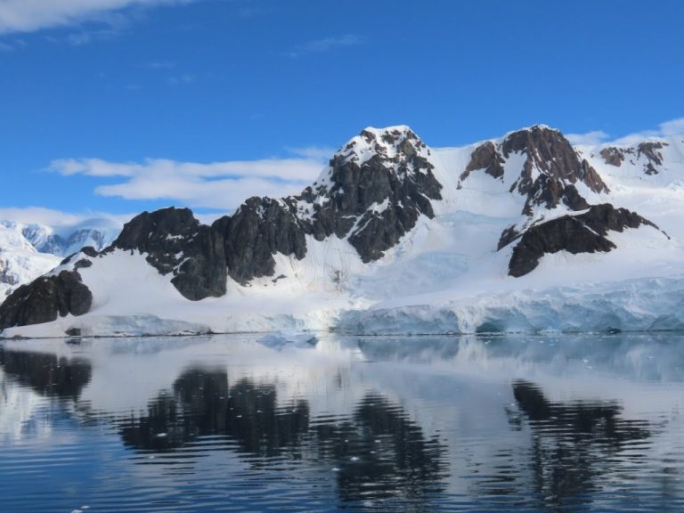 Craggy snow-covered rock is reflected in the calm blue water of the Antarctic Peninsula. Views like this made our scenic Antarctica cruise feel every bit as extraordinary as I had dreamed.