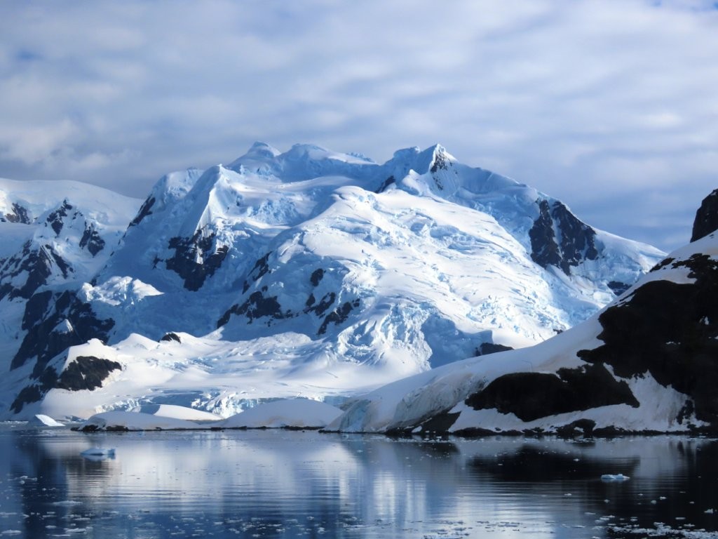A sweeping Antarctic coastline reflects the brilliant white snow, reflected in the vivid blue water. 