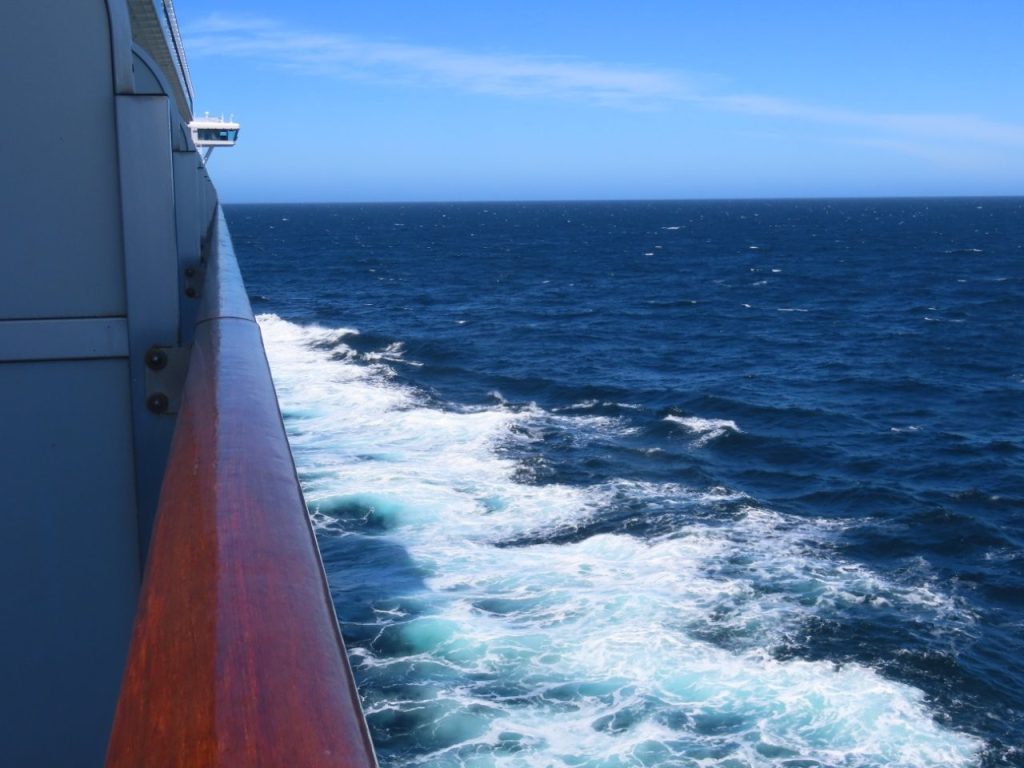 White foam trails alongside a cruise ship as it sails across deep blue ocean under clear skies. This view captures what much of our Drake Passage crossing looked like on the way to Antarctica.