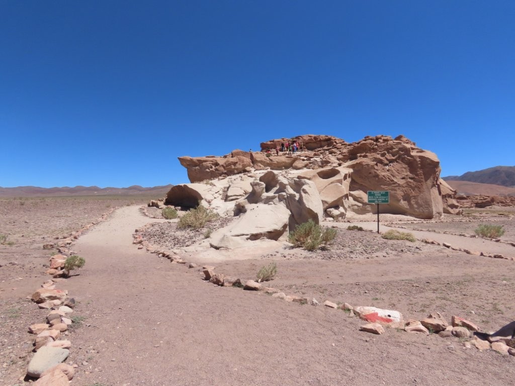 A dusty walking path circles a low sandstone outcrop in an open desert plain beneath an intensely blue sky. With almost no signs or map, I wandered among the rocks unsure where the important carvings were located.