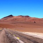 A narrow paved highway disappears into rolling red hills beneath an endless blue sky. One of the joys of visiting the Atacama Desert is simply driving through landscapes that seem to go on forever.