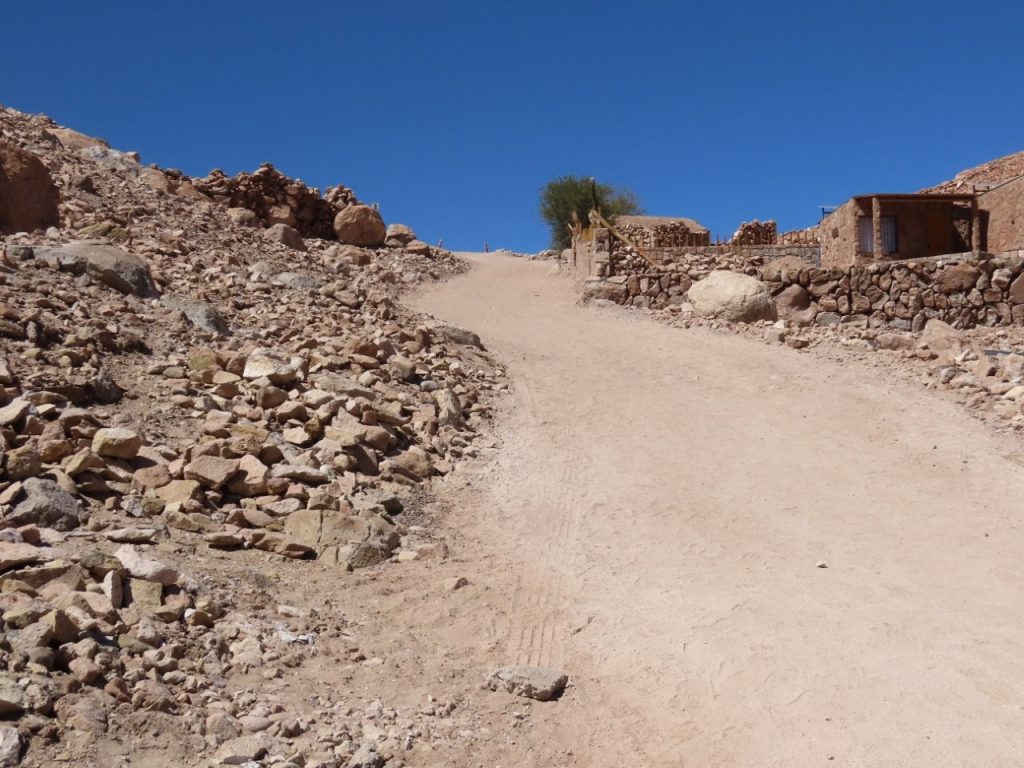 A steep dusty road climbs between loose rocks and simple stone walls toward the parking area above. The walk back up was the hardest part of Valle de Jere, and I felt dizzy halfway to the top.