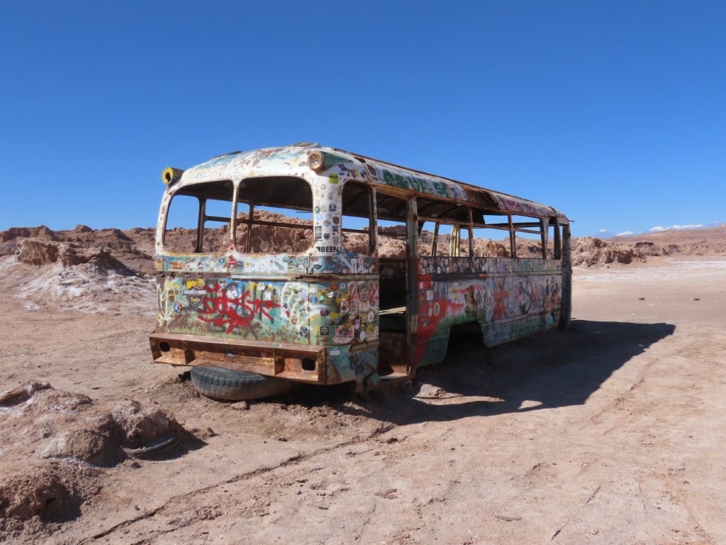 Sunlight shines through the empty frame of a weathered bus coated in travel stickers from around the world. Visitors often stop here to stretch their legs and add a fun photo opportunity to a day exploring the desert.