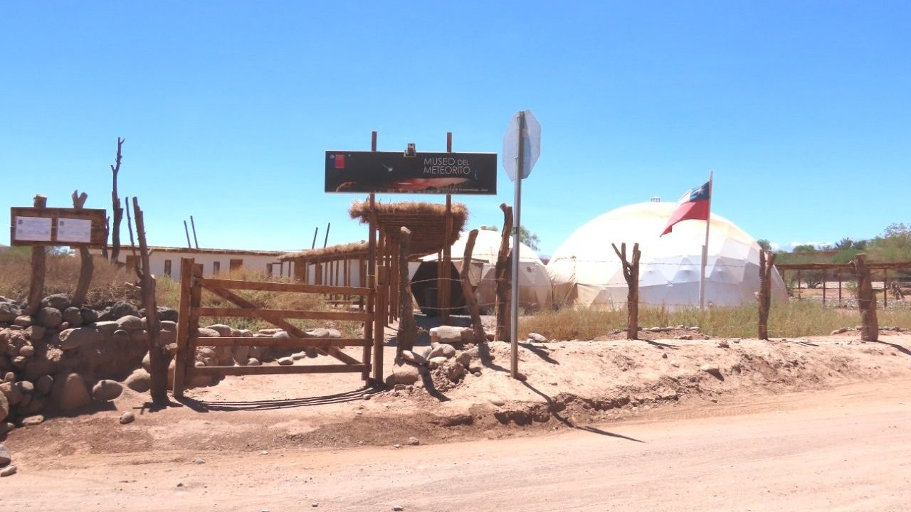 A roadside entrance sign welcomes visitors to the Meteorite Museum, with dome-shaped structures visible behind the gate. Attractions like this offer a fascinating look at the Atacama Desert's connection to astronomy and space science.