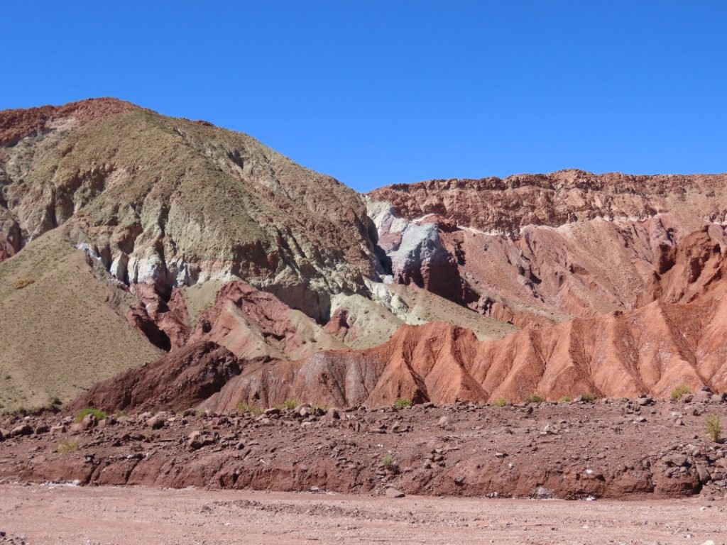 Rounded mountain slopes rise in broad bands of rust red, muted green, cream, and pale lavender beneath a deep blue sky. The colors were earthy rather than bright, but the layers looked as though different mountains had been pushed together.