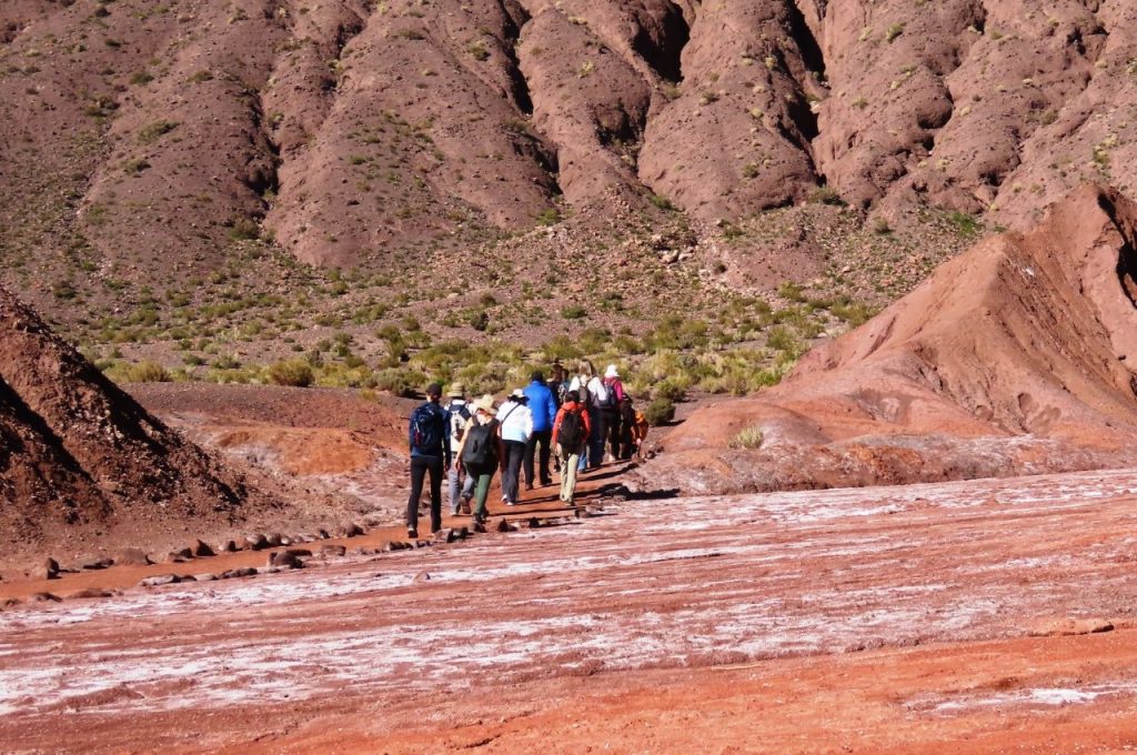 A group of tourists walk single-file into the Rainbow Valley. Guided tours help visitors understand the geology and colorful mineral deposits that make Rainbow Valley unique.