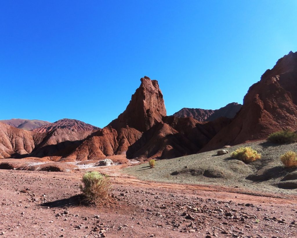 A dark red peak rises up against a brilliant blue sky at the end of the road inside Rainbow Valley Atacama. 