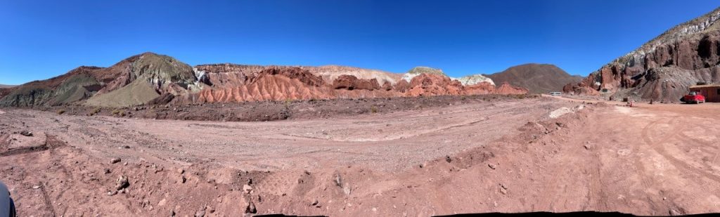 A broad panorama stretches across red, brown, pale green, and white hills under an uninterrupted blue sky. The changing colors, wildlife, and remote roads made Rainbow Valley Atacama one of our most memorable drives from San Pedro.