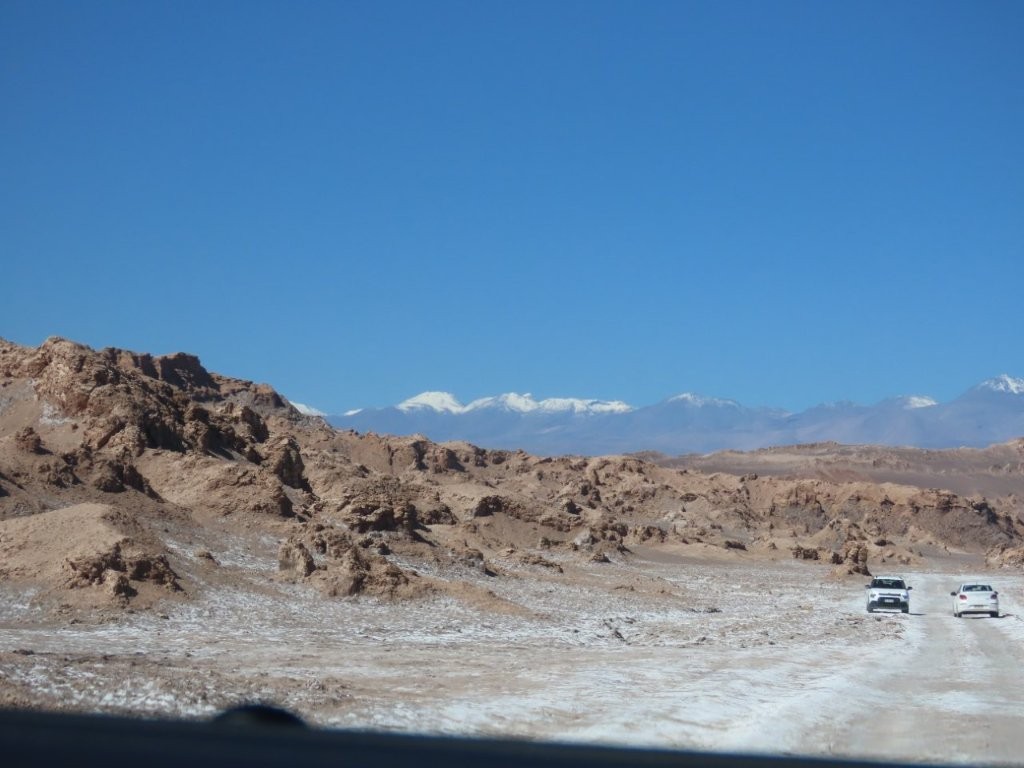 A rough and bumpy leads through the gray desert as cars pass each other up ahead.