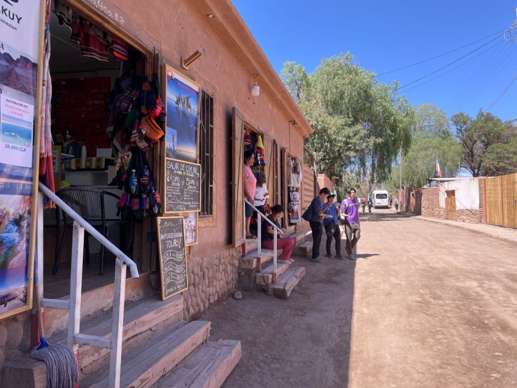Small tour offices and local businesses line a quiet dirt street beneath a bright desert sky. Exploring San Pedro de Atacama on foot is one of the best ways to get a feel for the town's relaxed atmosphere.