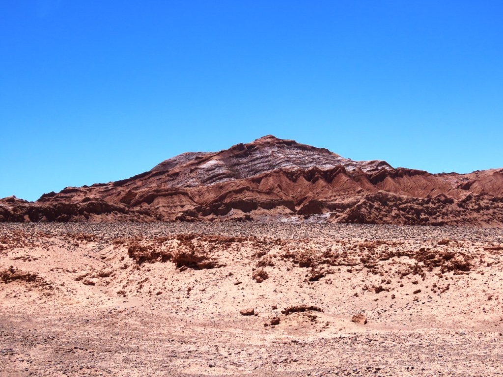 Rugged red and white mineral-streaked hills rise above a barren desert landscape. Centuries of wind and geological activity have sculpted some of the region's most dramatic scenery.