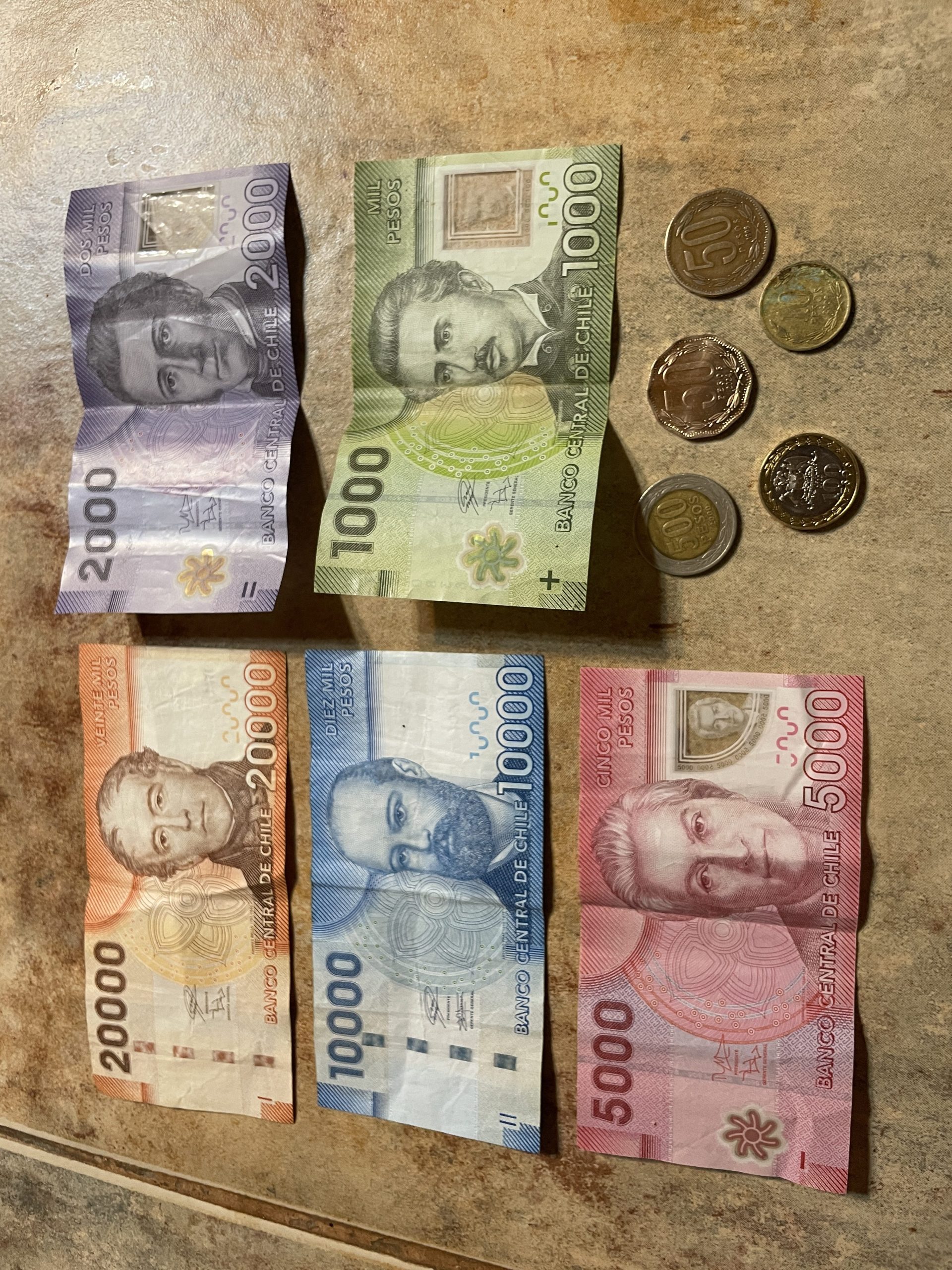 Colorful Chilean peso banknotes and coins are displayed on a tabletop, showing several common denominations used throughout the country. Understanding the local currency can make traveling through Chile easier and more convenient.