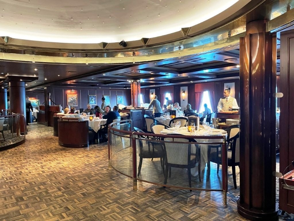 Diners sit at white-tablecloth tables surrounded by dark wood inside Crown Grill aboard Sapphire Princess. Cruise beverage packages can include benefits beyond drinks, so specialty dining matters when comparing what each package actually offers.