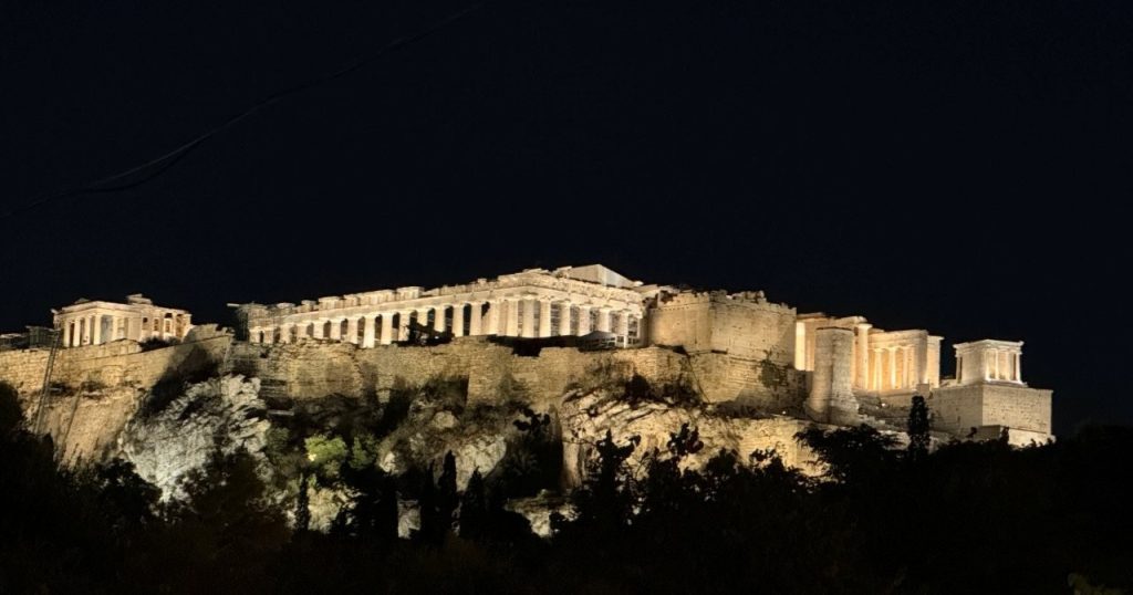 The illuminated Acropolis and Parthenon glow golden against the black night sky above Athens. Seeing the Acropolis lit after dark was one of the most memorable moments of our evening walking tour.
