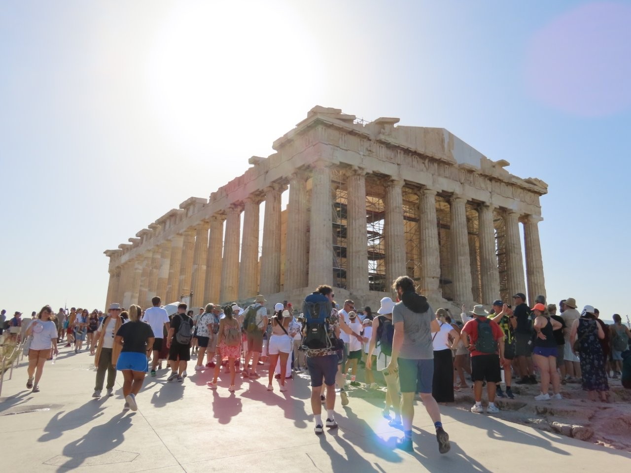 The weathered marble columns and triangular pediment of the Parthenon stand above a crowd of visitors on the Acropolis. Standing in front of the Parthenon was the highlight of our Athens itinerary 2 days of sightseeing.