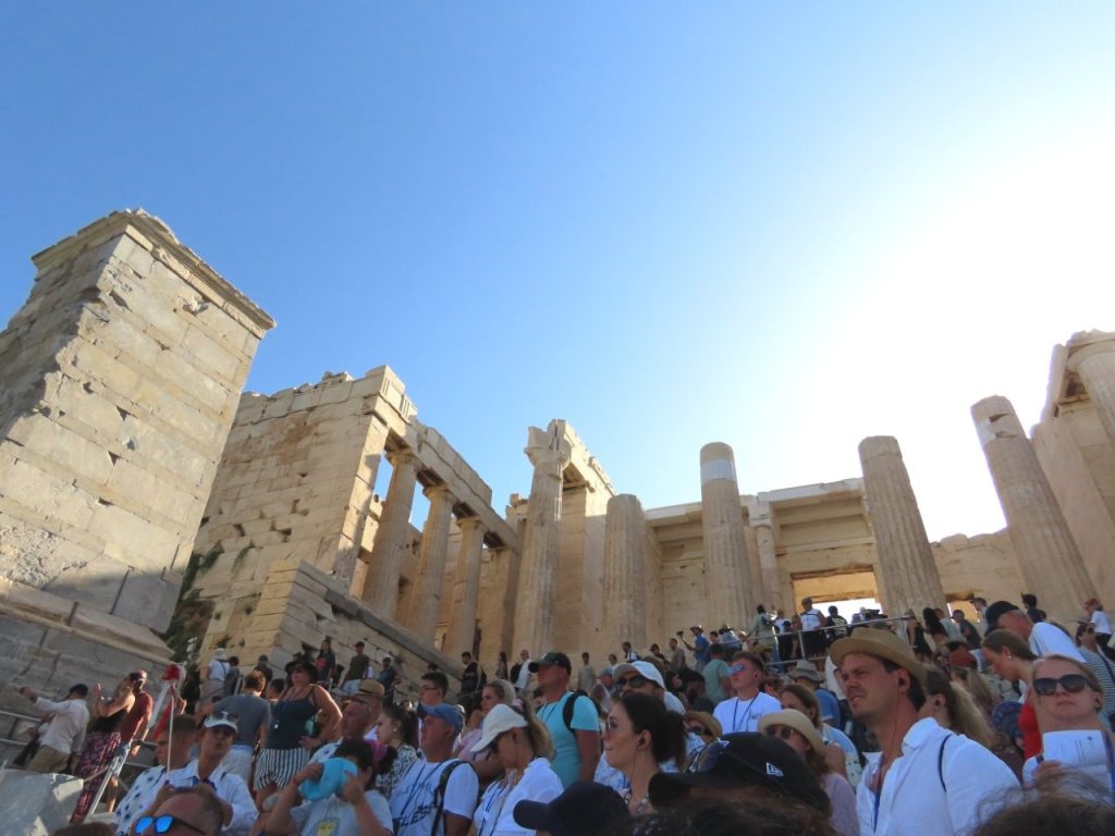 Crowds climb through the towering marble columns of the Propylaea entrance to the Acropolis under a cloudless blue sky. The busy gateway shows how the crowds increased as we approached the top during our morning tour.