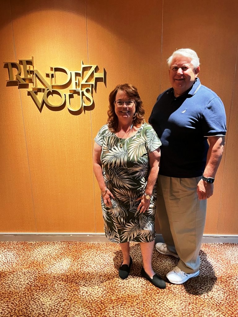 Kari and Bill pose together aboard Celebrity Infinity on Chic Night, with Kari dressed up for the evening and Bill wearing a collared shirt. Their polished but comfortable outfits reflect the range of clothing worn for an evening aboard the cruise ship.