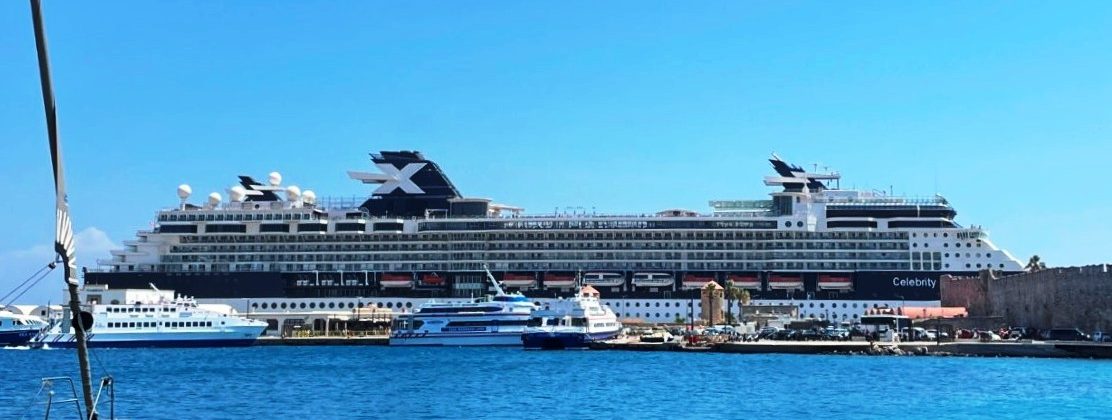 Celebrity Infinity stretches across the blue water beneath a clear sky, its white hull and rows of decks visible from shore. The ship served as both Kari and Bill’s hotel and transportation while they sampled several destinations around Greece.