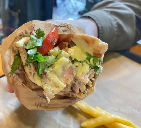 A pita wrapped gyro sandwich with chicken, lettuce, tomatoes and french fries.