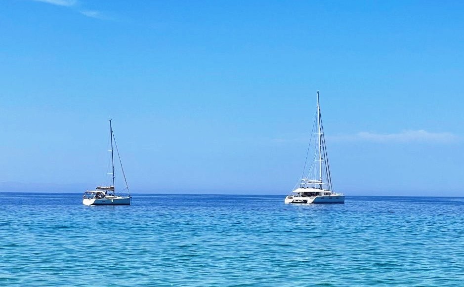Clear turquoise Aegean water shimmers over rounded rocks visible beneath the surface near Mykonos. The remarkable clarity and color show why Greece’s blue water became one of Kari’s lasting memories from the trip.