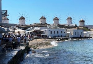 White cylindrical windmills topped with thatched roofs stand against a brilliant blue sky above Mykonos. The windmills, whitewashed lanes and blue water gave us the classic Greek-island scenery I had been waiting for.