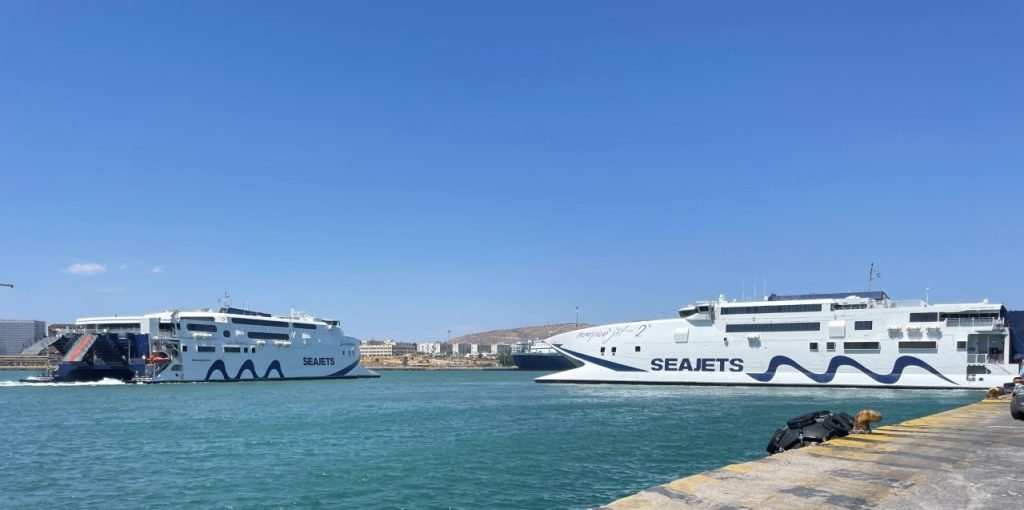Large passenger ferries cross the bright blue harbor beside the concrete wharf at Piraeus Port. The waterfront reflects the very different purpose of our pre-cruise stay: being close to the port and ready for embarkation.