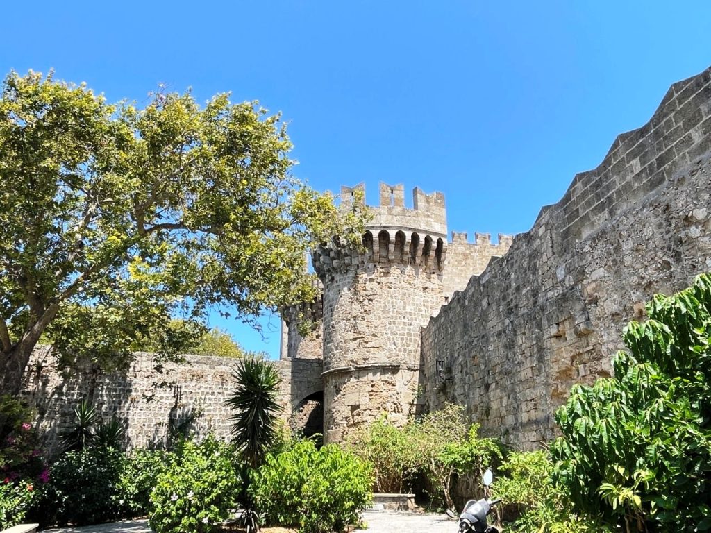 Stone towers and crenellated medieval walls rise above leafy trees beneath a brilliant blue sky in Rhodes Old Town. The remarkably preserved historic center was easy to explore independently from the Celebrity Infinity cruise port.