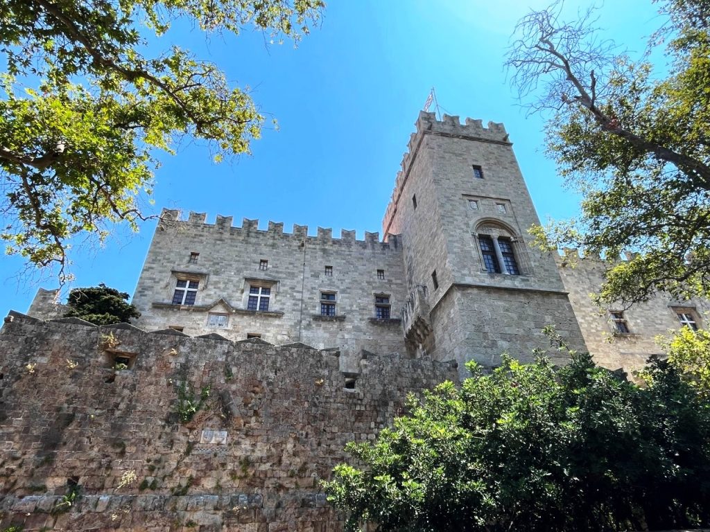A stone tower rises above the medieval walls and leafy streets of Rhodes Old Town beneath a bright blue sky. Rhodes is where Kari particularly noticed how much more common public cigarette smoking seemed compared with what she encounters at home.