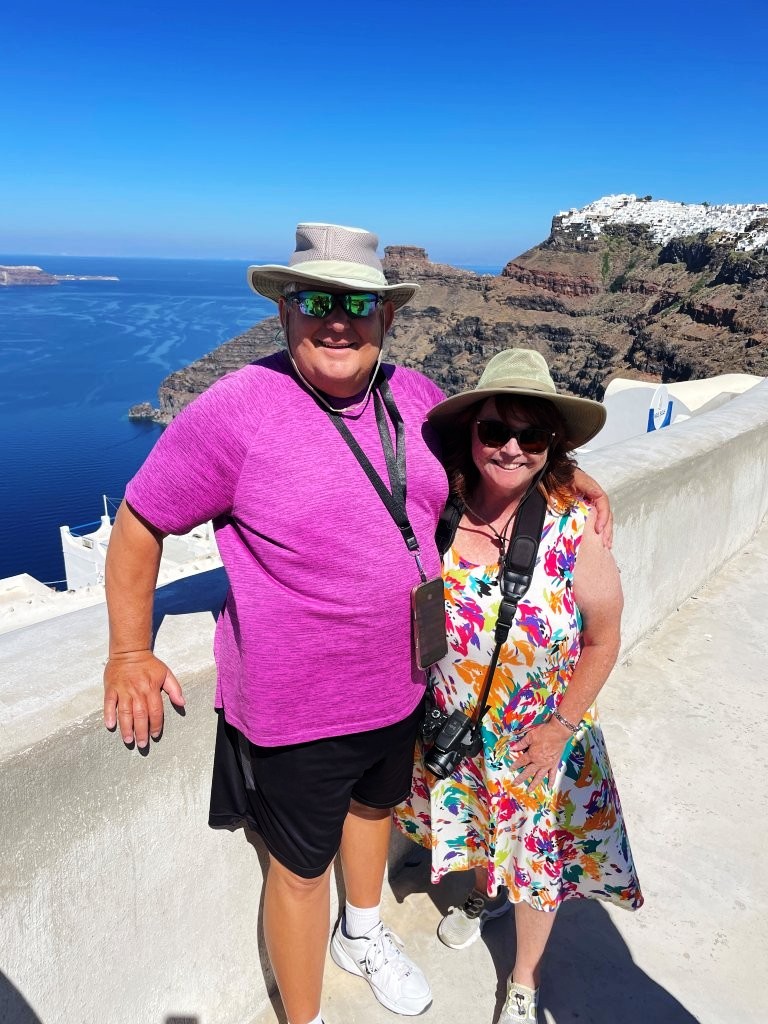 Kari and Bill stand together above Santorini’s dramatic caldera with brilliant blue Aegean water and rugged islands stretching behind them. Their firsthand travels through Athens and the Greek islands are the experience behind the practical advice throughout this Greece travel guide.