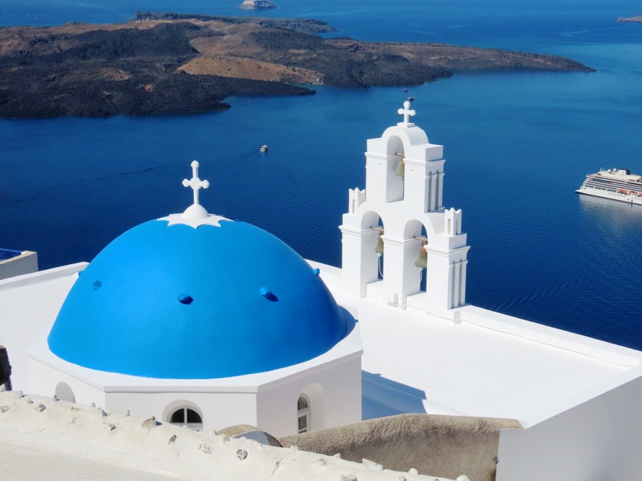 A brilliant blue dome and white bell tower rise above Santorini’s deep-blue caldera under a cloudless sky. This iconic Greek island view introduces the Greece travel guide and the practical tips first-time visitors need before their trip.