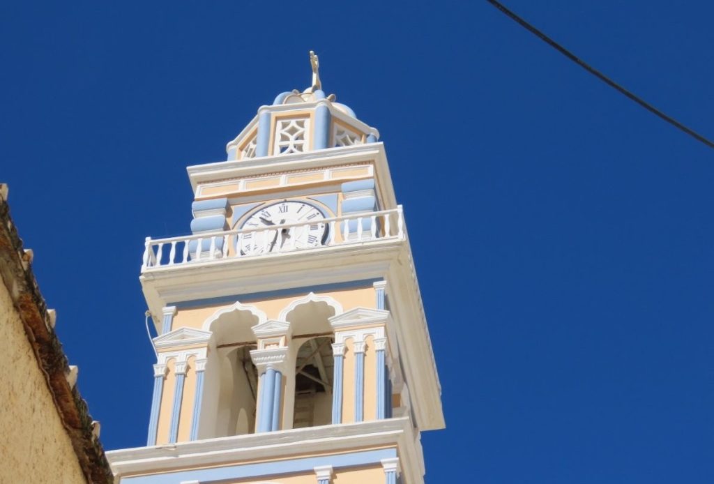 An ornate cream-and-white bell tower rises dramatically into a deep cobalt-blue Santorini sky. Architectural details throughout the island made the Santorini port day about much more than just the famous caldera views.