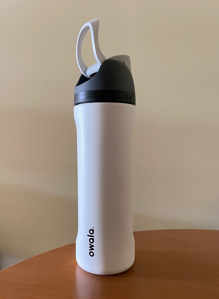 An insulated Owala water bottle with a covered FreeSip lid sits ready to carry on a day of sightseeing. Keeping water cold made this bottle especially useful during long days exploring Greece in the heat.