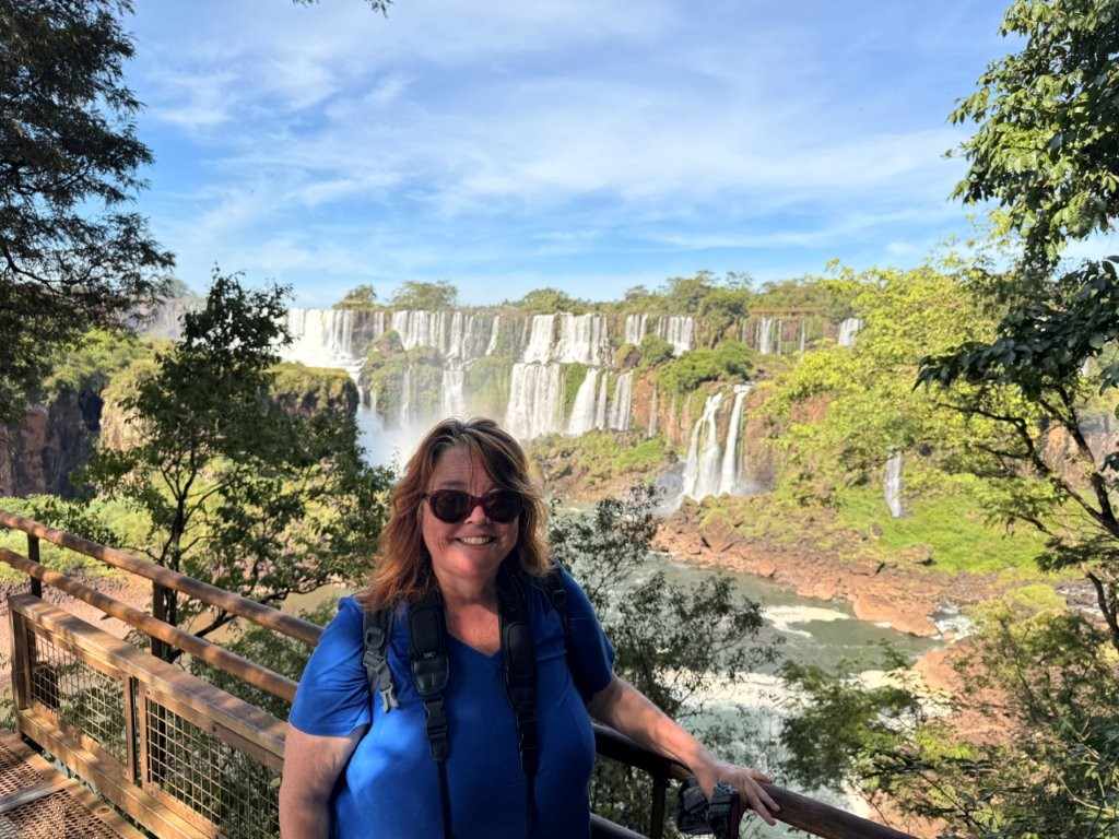 Kari smiles at a viewing platform with the enormous Iguazú Falls stretching across the landscape behind her in Argentina. Exploring South America is one of the experiences that reflects how far she's come since her early travel anxiety.