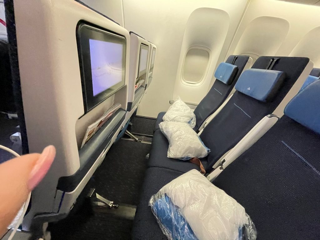 Three dark blue airplane seats with headrests and white pillows sit beside the cabin windows, with entertainment screens mounted on the seats ahead. Everyone has different preferences, and finding the seat that feels most comfortable to you is part of learning how you like to travel.