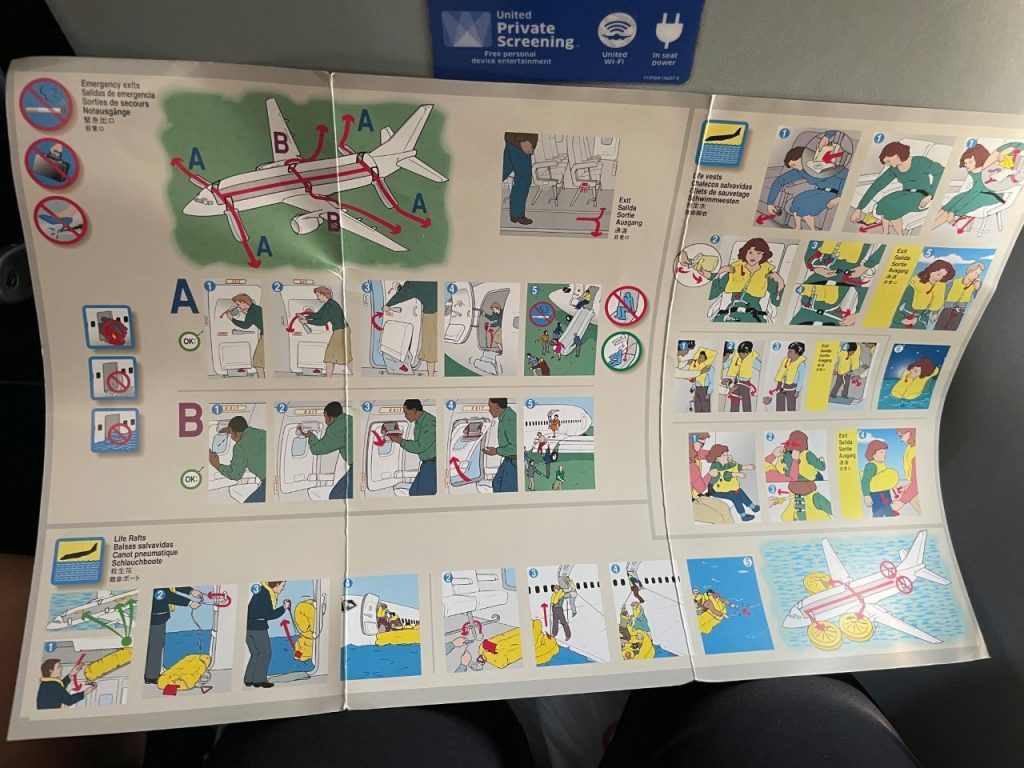 An unfolded airline safety card displays colorful diagrams of airplane exits, seat belts, emergency procedures, and passenger safety instructions. Even after many years of flying, I appreciate having those visual reminders available whenever I'm on an unfamiliar airplane.
