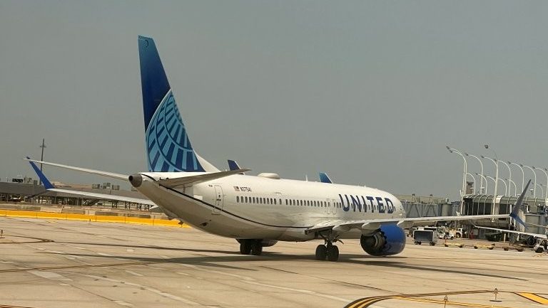 A white airplane with a blue tail taxis down the tarmac at the airport.