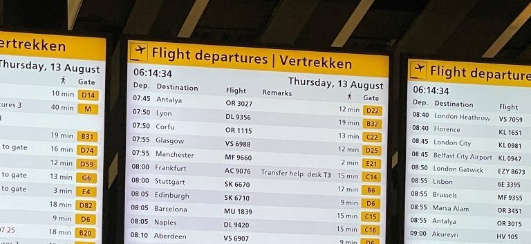 Three large airport departure screens display columns of flight numbers, destinations, departure times, and gate assignments in yellow and black. Although all those numbers and abbreviations may look confusing at first, you'll soon recognize these screens as one of the most useful features in an airport.