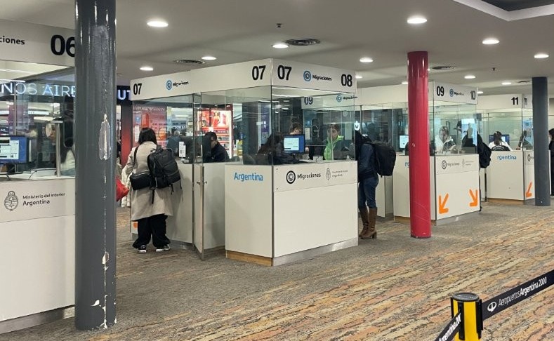 Travelers stand at numbered airport processing counters separated by glass partitions, with bright overhead lighting and red columns in the background. This stage may feel especially unfamiliar on your first international trip, but the airport staff are accustomed to helping passengers from all over the world.
