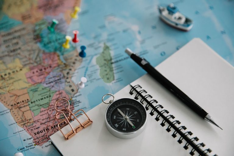 A map, a notebook with a blank page and a compass are the tools for how to plan a trip.