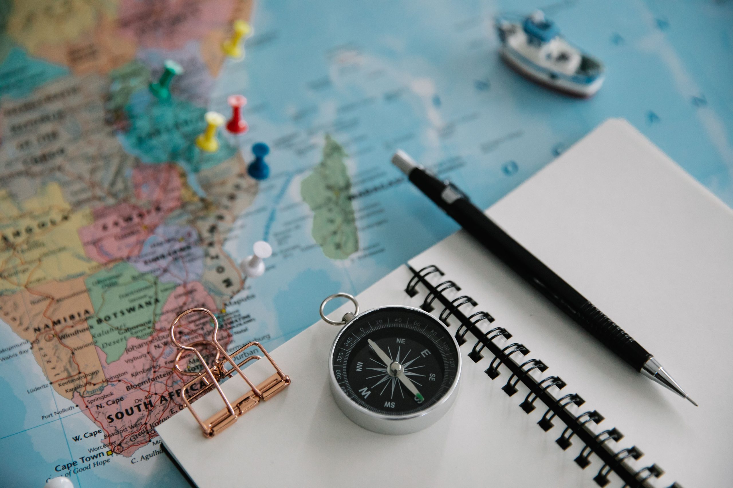 A map, a notebook with a blank page and a compass are the tools for how to plan a trip.